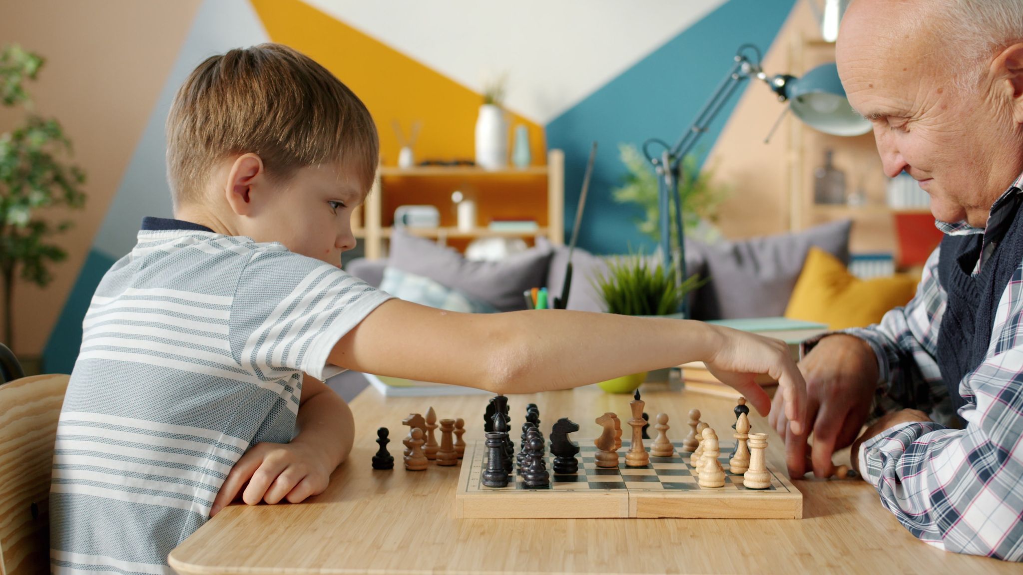 A grandfather and grandson play chess at home, focusing on strategy and bonding.