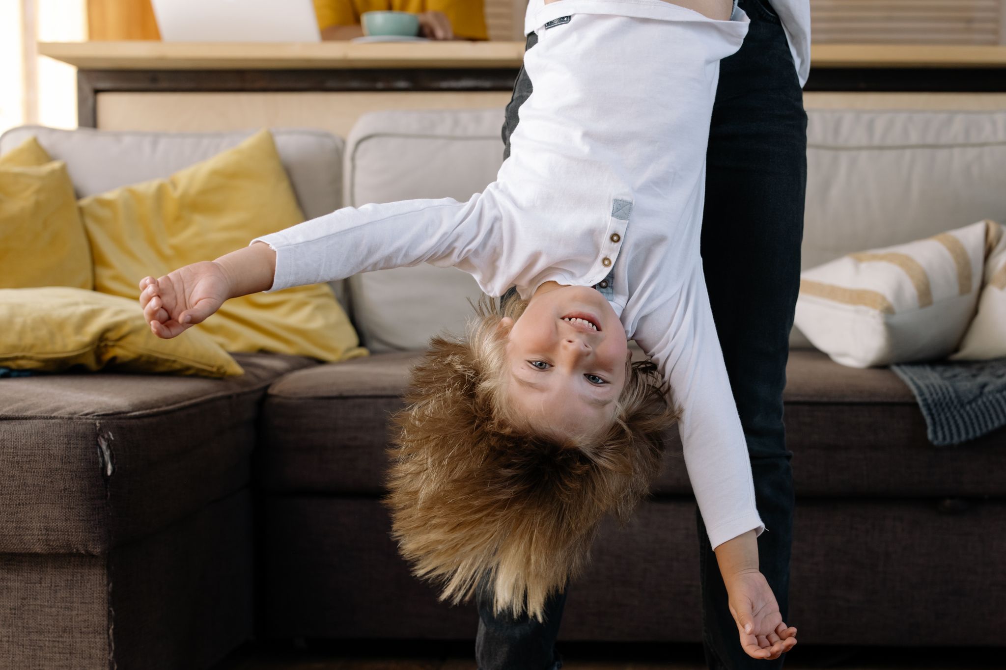 A happy child playfully hangs upside down over a couch, exhibiting joy and fun indoors.